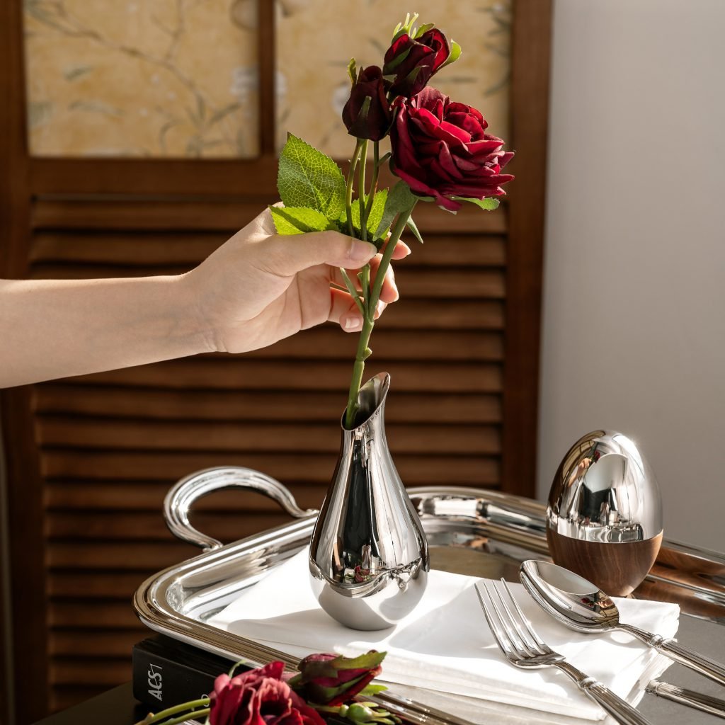 Steel Petit Vase (SS-39) featuring a miniature mirror-polished cylindrical body holding a delicate single stem, showcased as a Luxury Mirror Polished Desktop Vessel.