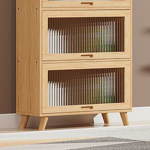 A 77-inch tall Natural Wood Bookcase in a warm oak grain finish. Features three tiers protected by upward-opening Fluted Glass Doors with black minimalist frames. This Ribbed Glass Bookshelf and Wooden Storage Organizer is shown in a bright contemporary setting, highlighting its sleek Flip-up Doors and easy-to-install board construction.