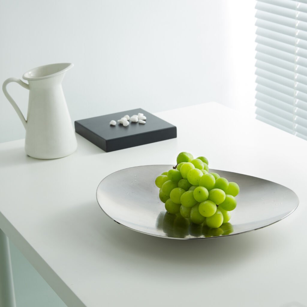 Steel Crinkled Bowl placed on a minimalist black glass table filled with vibrant green apples, representing Reflective High-End Artistic Vessel elegance.