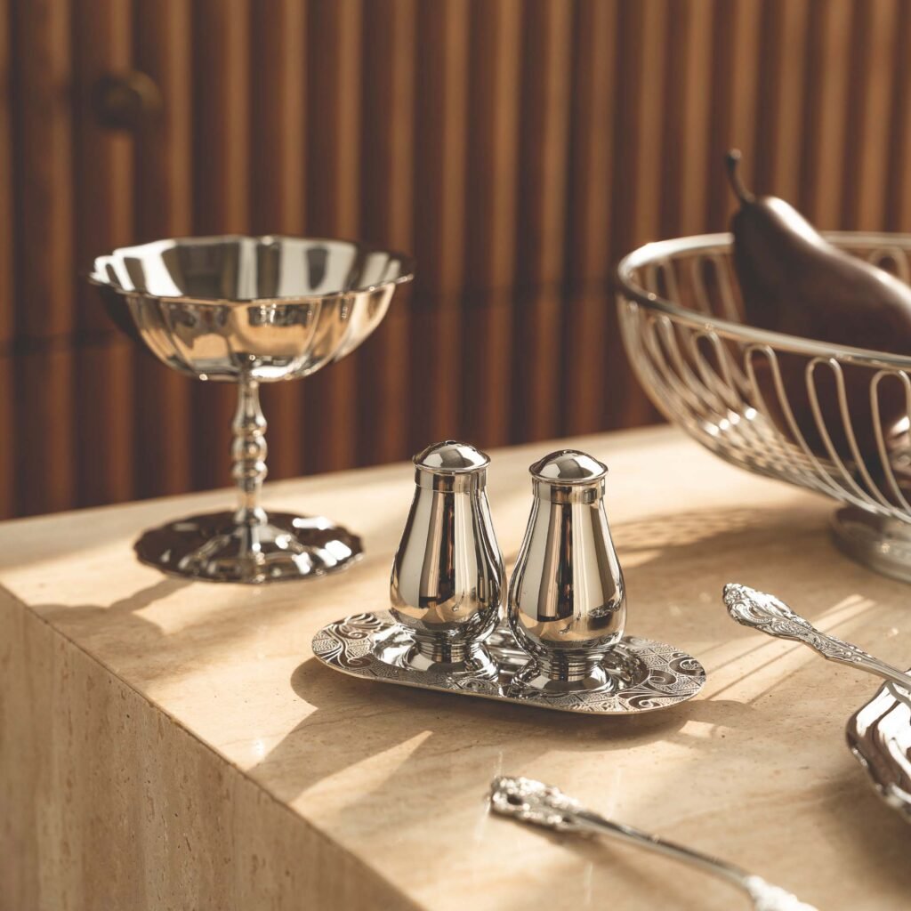 Steel Condiment Shaker placed next to a high-end induction cooktop, representing Reflective Minimalist Tableware for gourmet cooking.