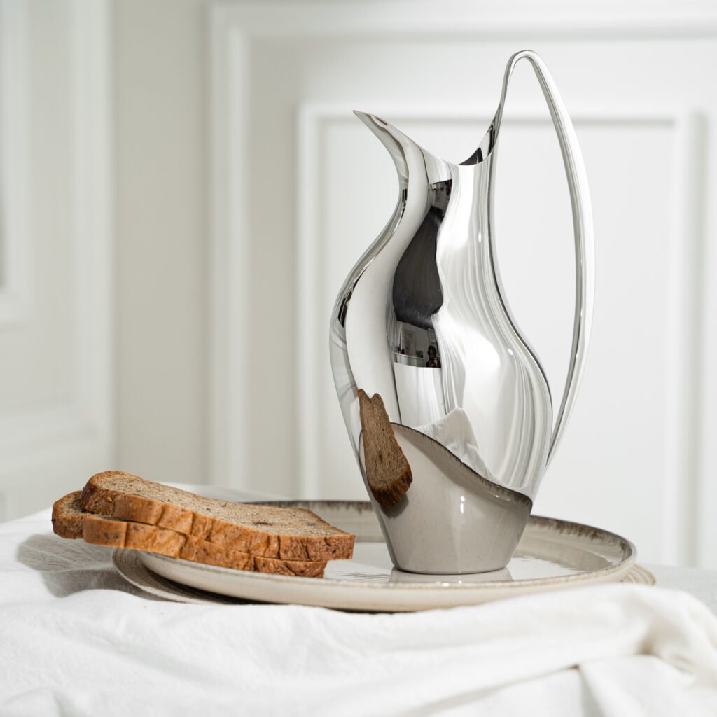 Close-up of the Modernist Avian Metalware, highlighting the elegant arch of the handle and the flawless, liquid-like reflection across the steel surface.