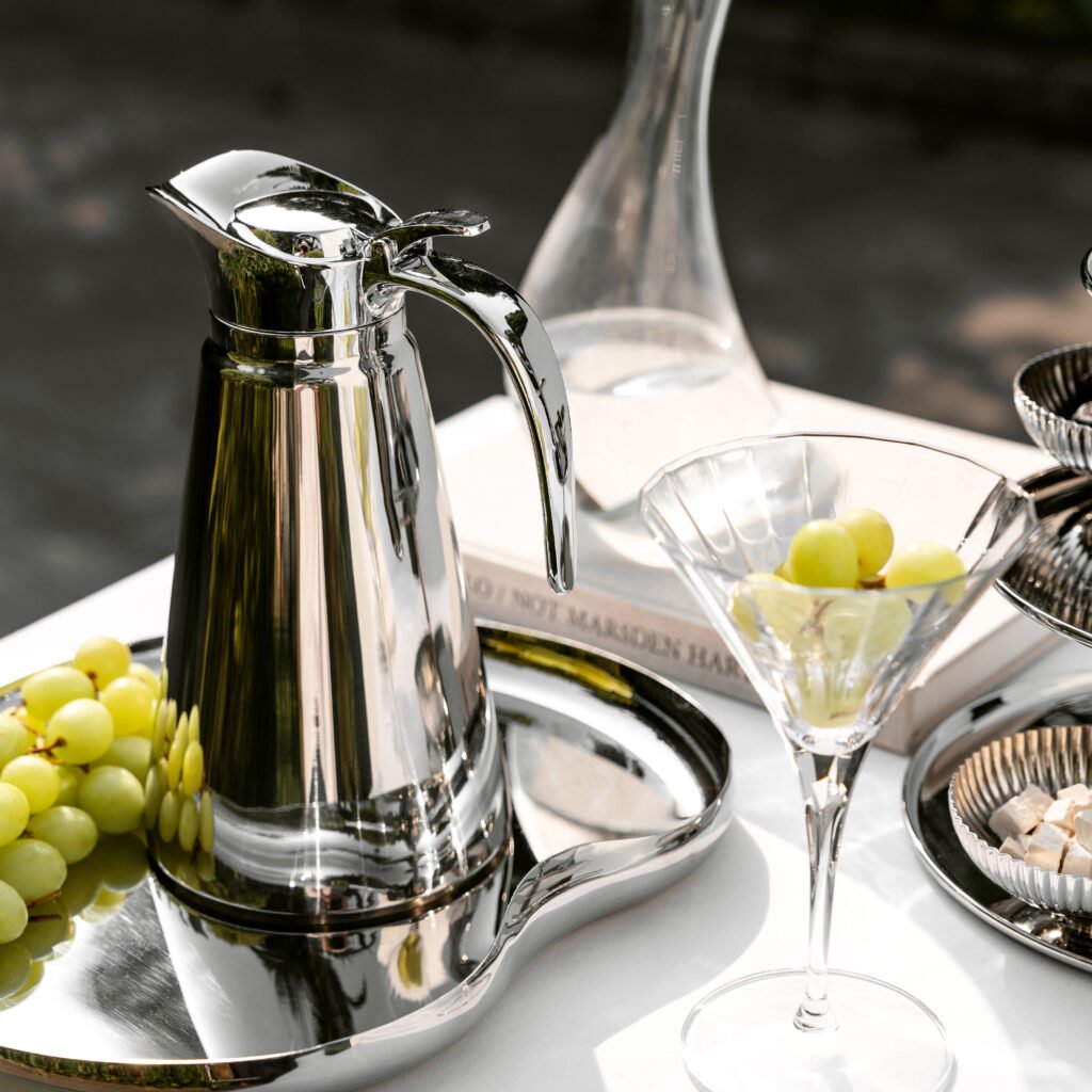 Steel Cylindrical Carafe placed on a dark slate executive desk beside a minimalist lamp, representing Reflective High-End Functional Art elegance.