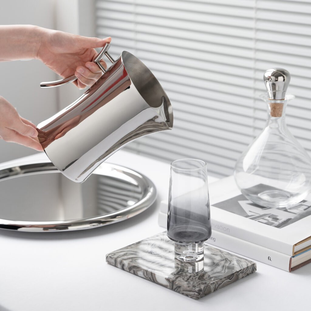 Steel Water Pitcher placed on a glass-topped terrace table beside fresh citrus, representing Reflective High-End Functional Art elegance.