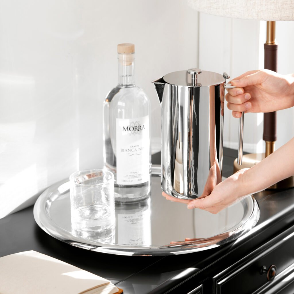 Steel Sculptural Pitcher placed on a dark slate boardroom table beside glass tumblers, representing Reflective High-End Functional Art elegance.