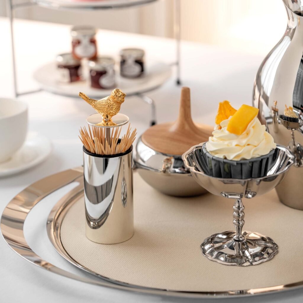 Steel Bird Toothpick holder standing on a minimalist dark wood surface, representing Reflective Whimsical Dining Art in a luxury setting.