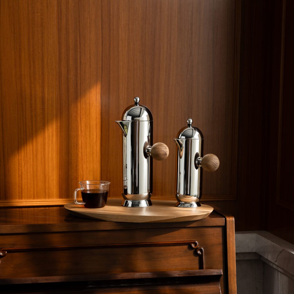 Steel Orb Pitcher placed on a back-lit glass bar counter beside crystal glassware, representing Reflective High-End Kinetic Sculpture elegance.