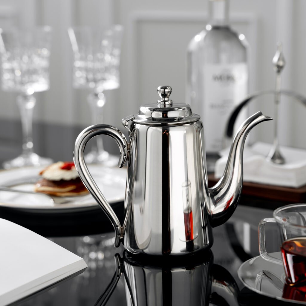 Steel Drip Kettle placed on a dark obsidian console with vibrant citrus, representing Reflective High-End Drip Art elegance.