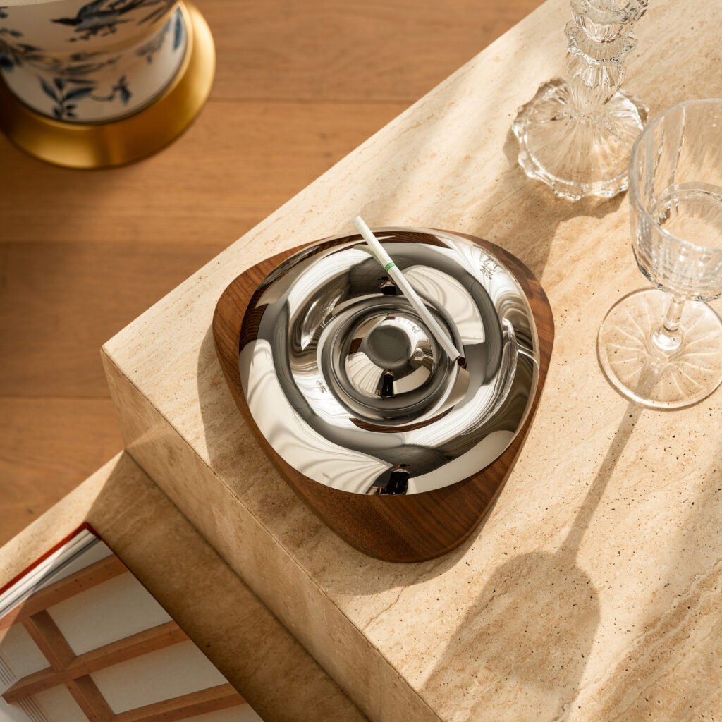 Steel Egg Ashtray placed on a minimalist black glass desk with a designer lighter, representing Reflective High-End Sculptural Art elegance.