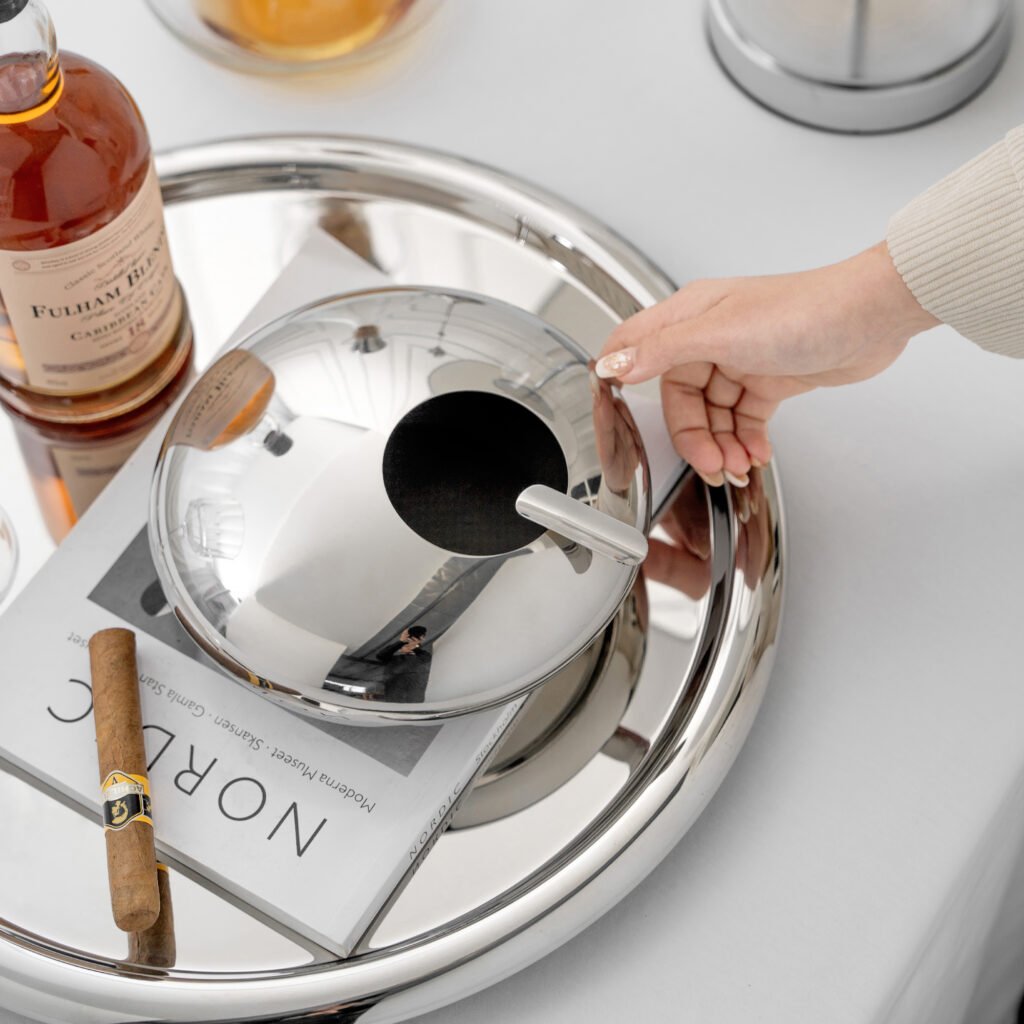Steel Square Ashtray placed on a heavy glass coffee table beside a modern architectural journal, representing Reflective High-End Architectural Art elegance.