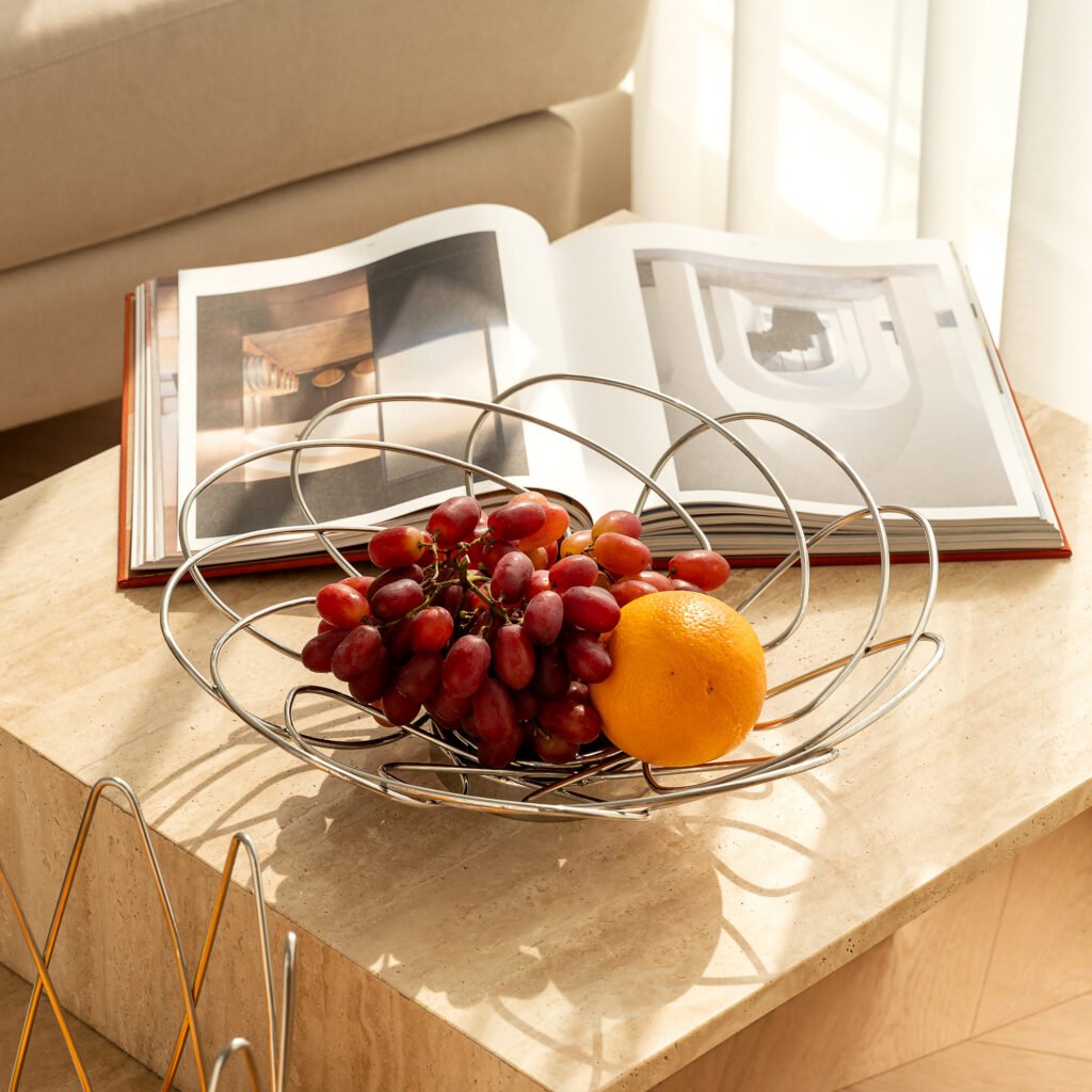 Steel Bud Basket placed on a white marble pedestal with exotic fruits, representing Reflective High-End Floral Art elegance.