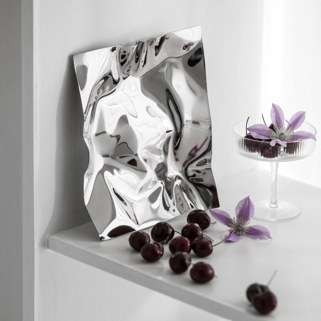 Steel Crinkled Bowl placed on a minimalist glass table with fresh citrus fruits, representing Reflective Organic Art Piece elegance.