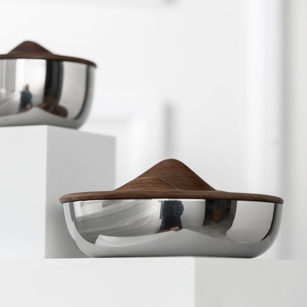 Close-up of the Modernist Topographic Metalware, highlighting the flawless panoramic reflection along the sharp, elegant curves of the steel mountain ridge.