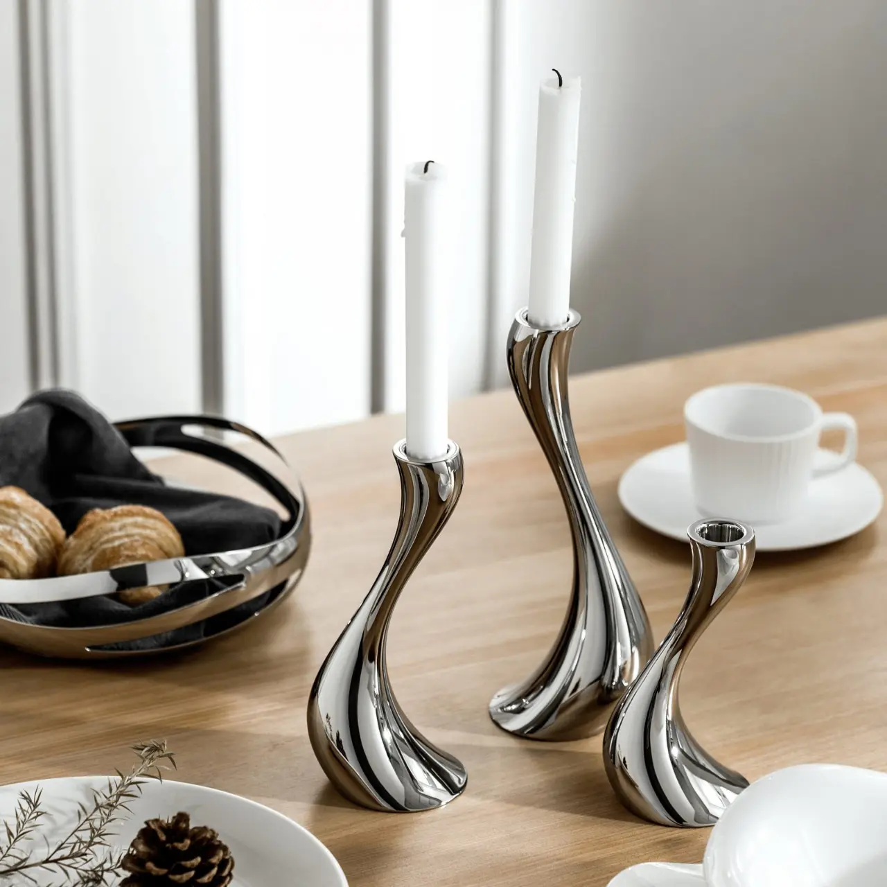Modern mirror-polished stainless steel S-curve candle holders with white taper candles set on a warm wooden dining table by Apexerahomelife.