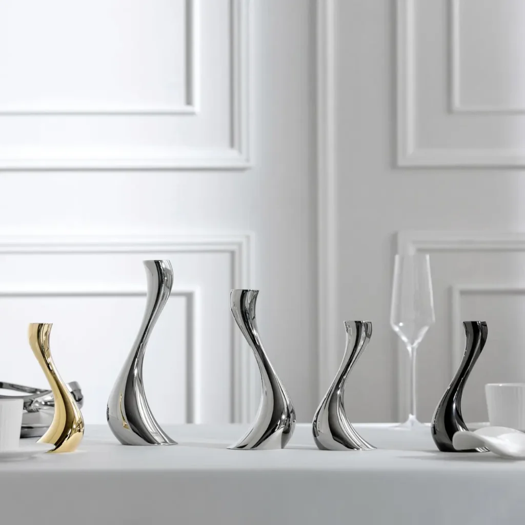 A lineup of stainless steel candle holders in gold and silver mirror finishes displaying various sizes against a clean white wall.