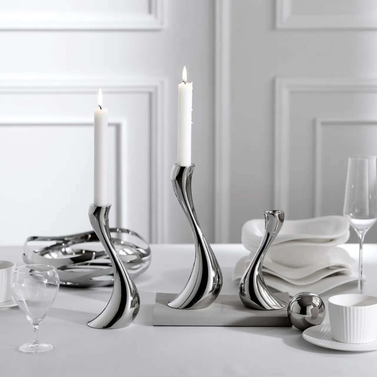 Elegant silver stainless steel candelabras holding lit white candles on a white tablecloth dining setting.