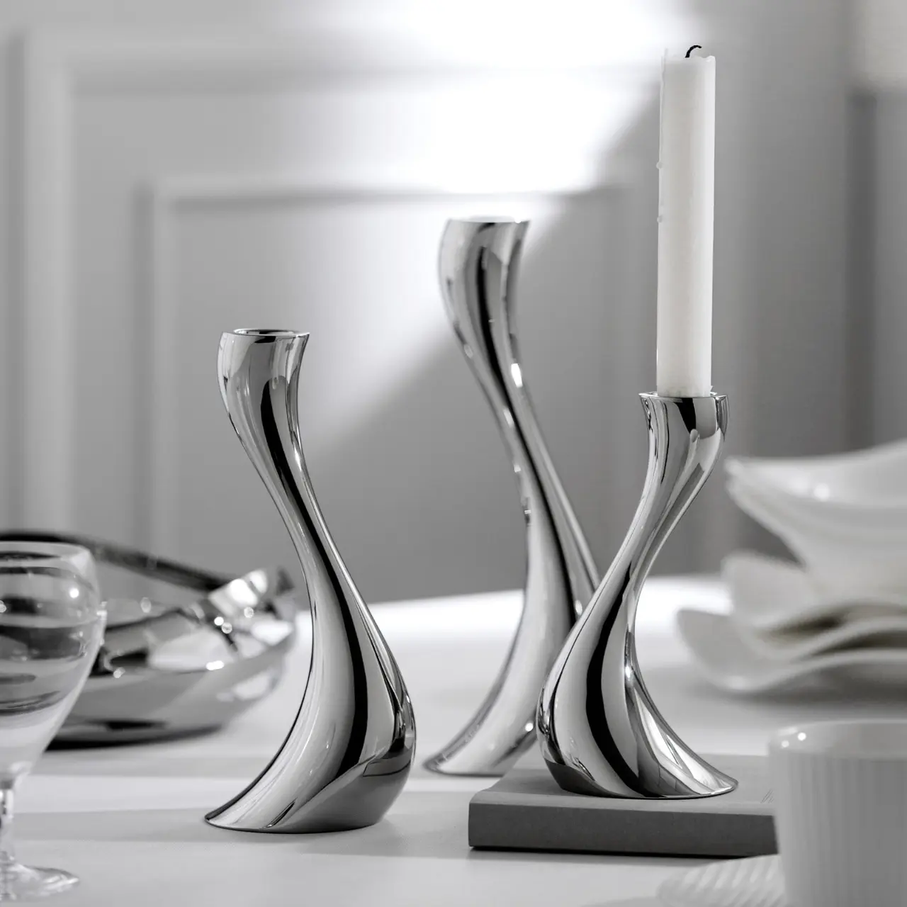 Close-up view of modern curved stainless steel candle holders with polished reflective surfaces on a dining table.
