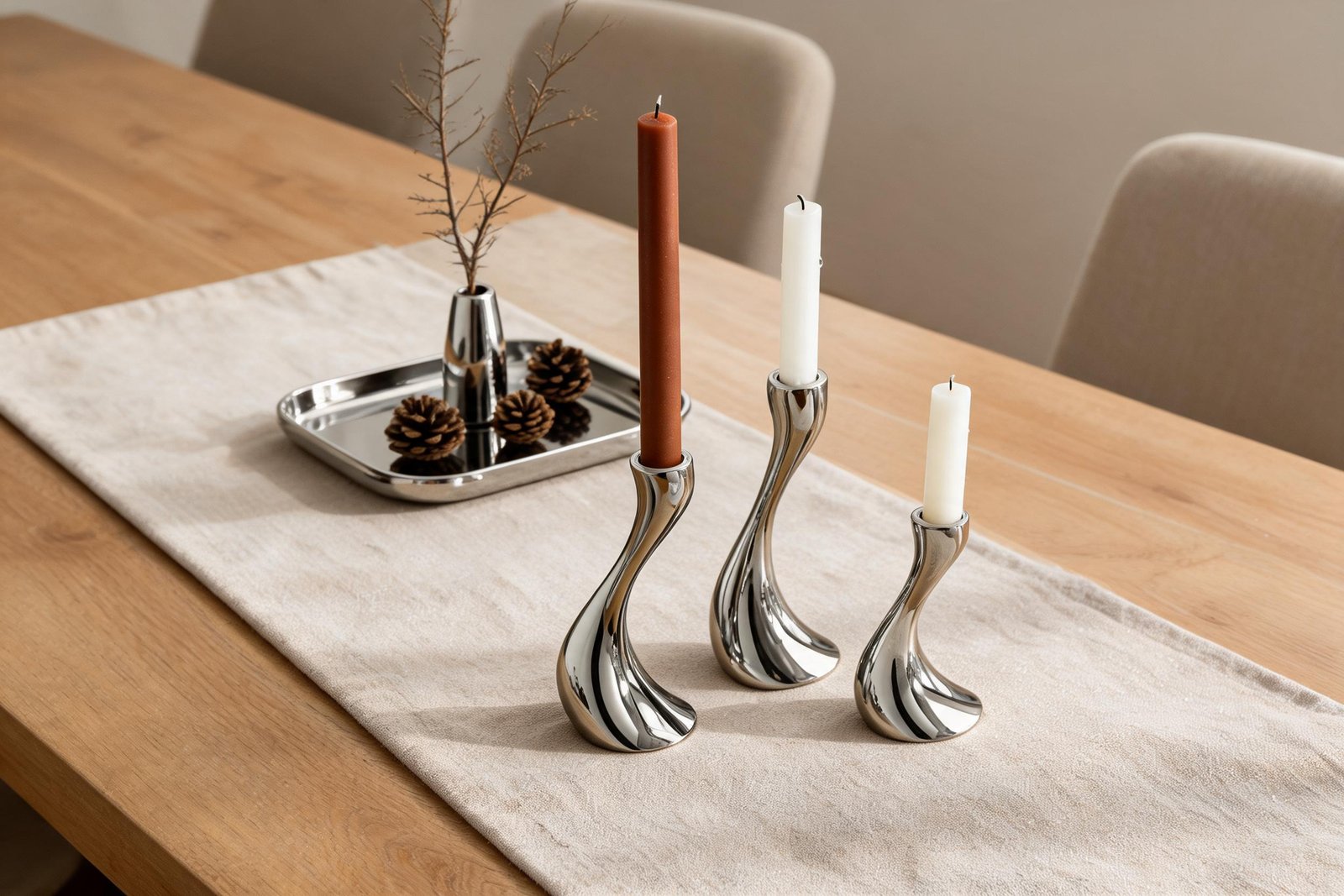 Fall candle holder centerpiece built from mirror polished stainless steel S-curve holders grouped off-centre on an oatmeal linen runner with rust and ivory tapers
