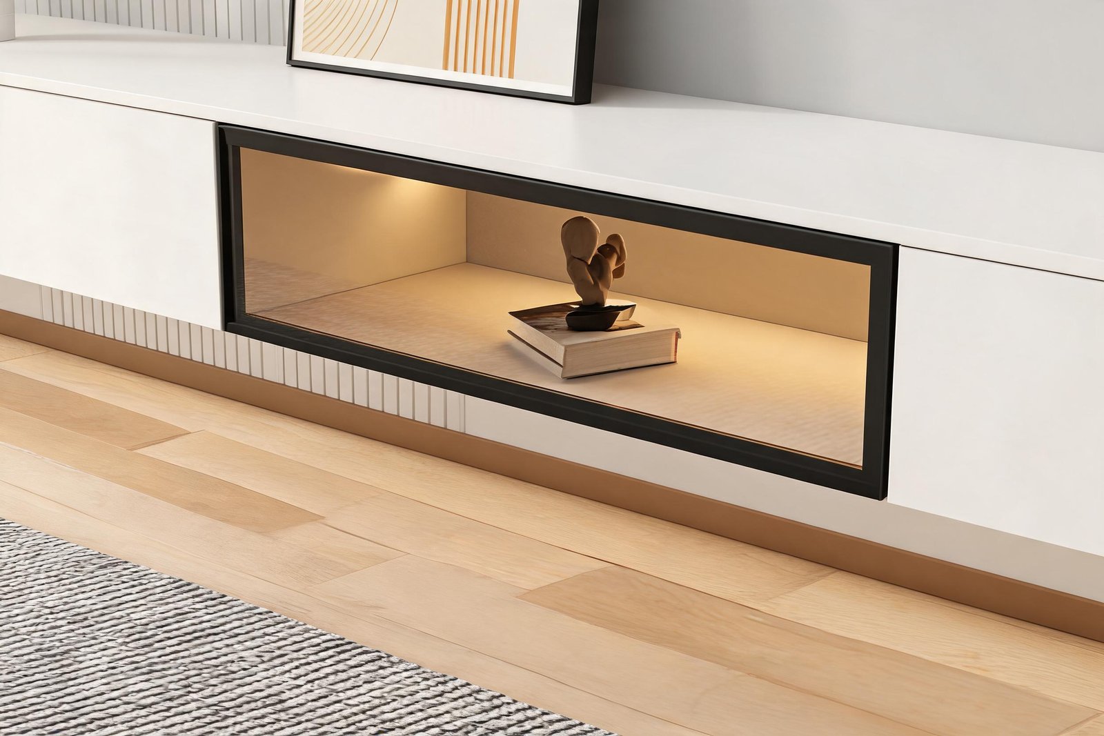 Detail of the slim black framed glass door and warm LED strip inside a white floating TV stand with LED lights, with a book and a sculpture in the lit compartment