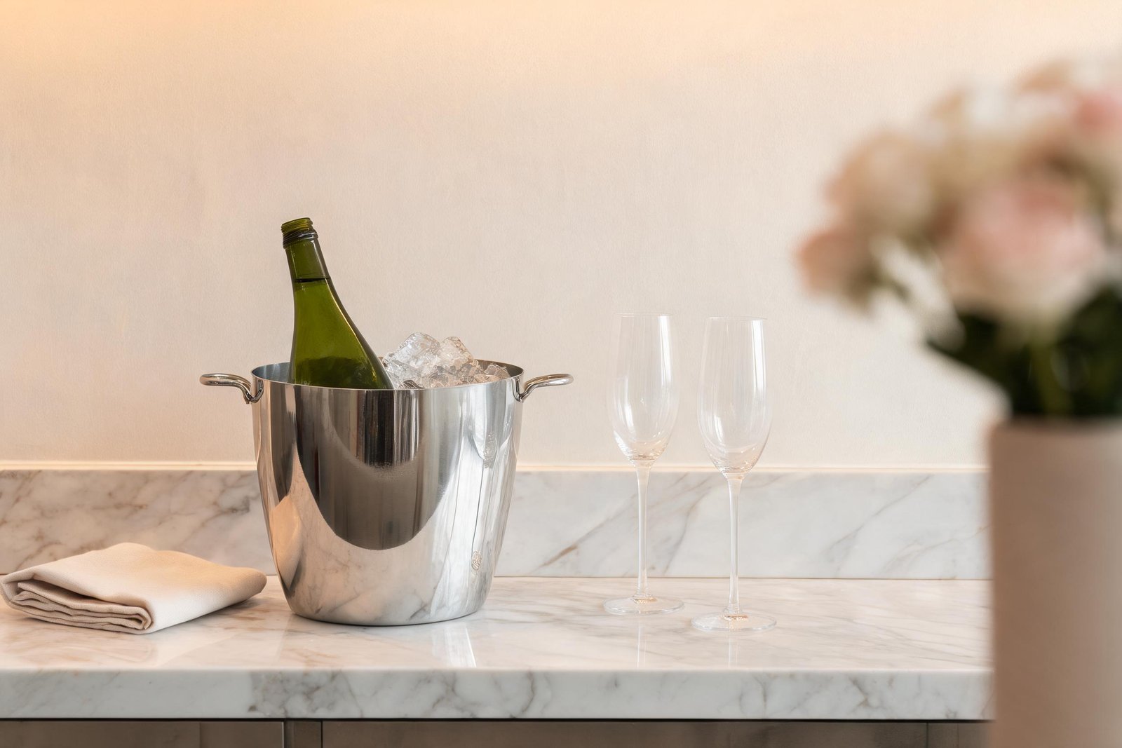 Home 29 Ice bucket sizes in use: a mirror polished tapered steel ice bucket holding a Champagne bottle and cubed ice on a pale marble bar top