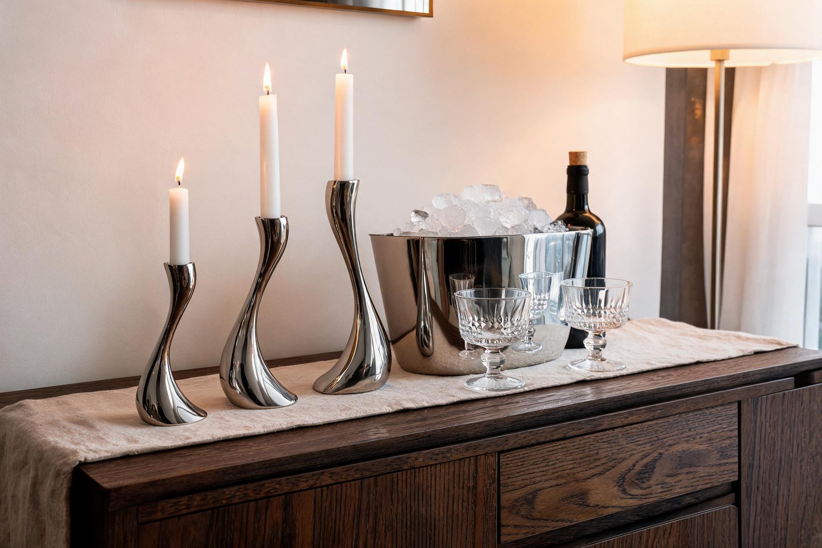 Thanksgiving drink station ideas: three S-curve mirror steel candle holders at low height beside the steel ice bucket, a wine bottle and two crystal glasses